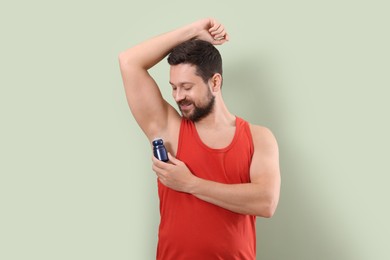 Smiling man applying roll-on deodorant on light green background