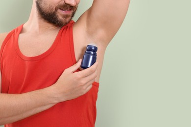 Photo of Man applying roll-on deodorant on light green background, closeup. Space for text