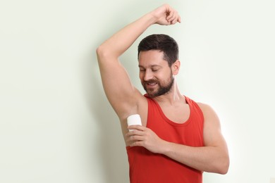 Smiling man applying solid deodorant on light green background. Space for text