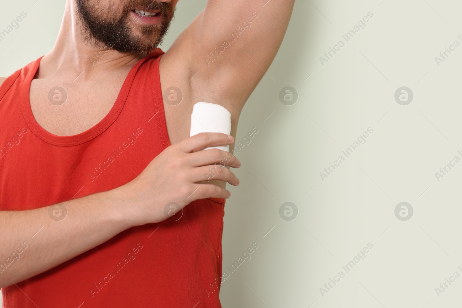 Photo of Smiling man applying solid deodorant on light green background, closeup. Space for text