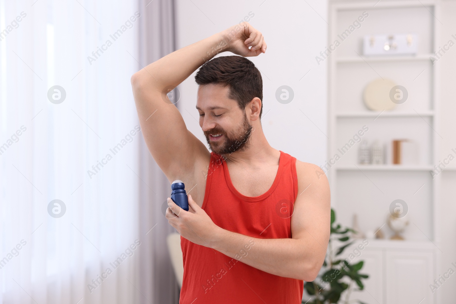 Photo of Smiling man applying roll-on deodorant at home