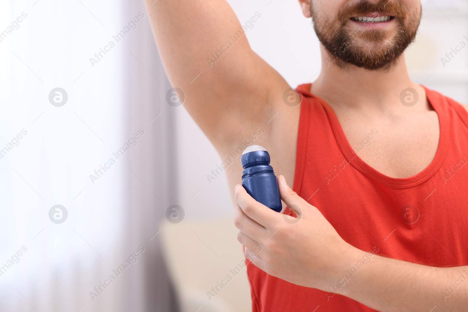 Photo of Smiling man applying roll-on deodorant at home, closeup. Space for text