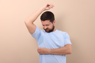 Emotional man in t-shirt before using deodorant on beige background