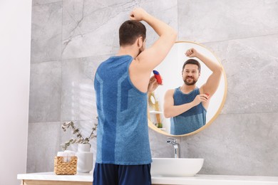 Smiling man applying solid deodorant near mirror at home, back view