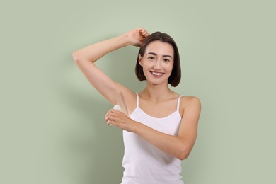 Smiling woman applying roll-on deodorant on green background