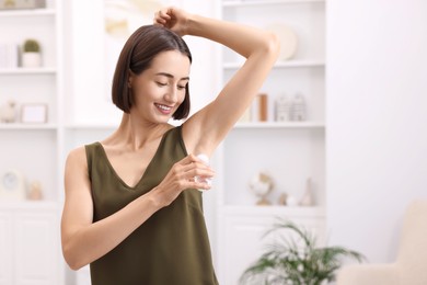 Photo of Smiling woman applying roll-on deodorant at home. Space for text