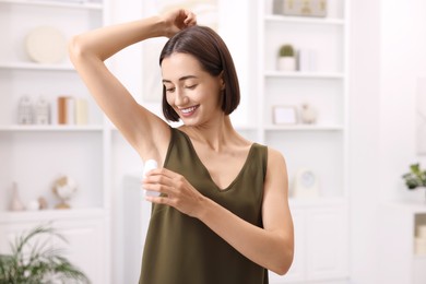 Smiling woman applying roll-on deodorant at home