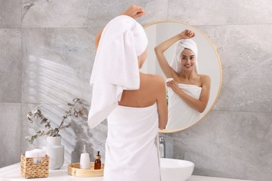 Smiling woman applying solid deodorant near mirror at home, back view