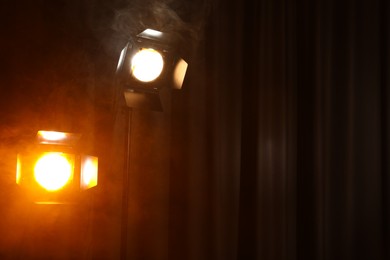 Photo of Professional spotlights against curtain in darkness. Space for text