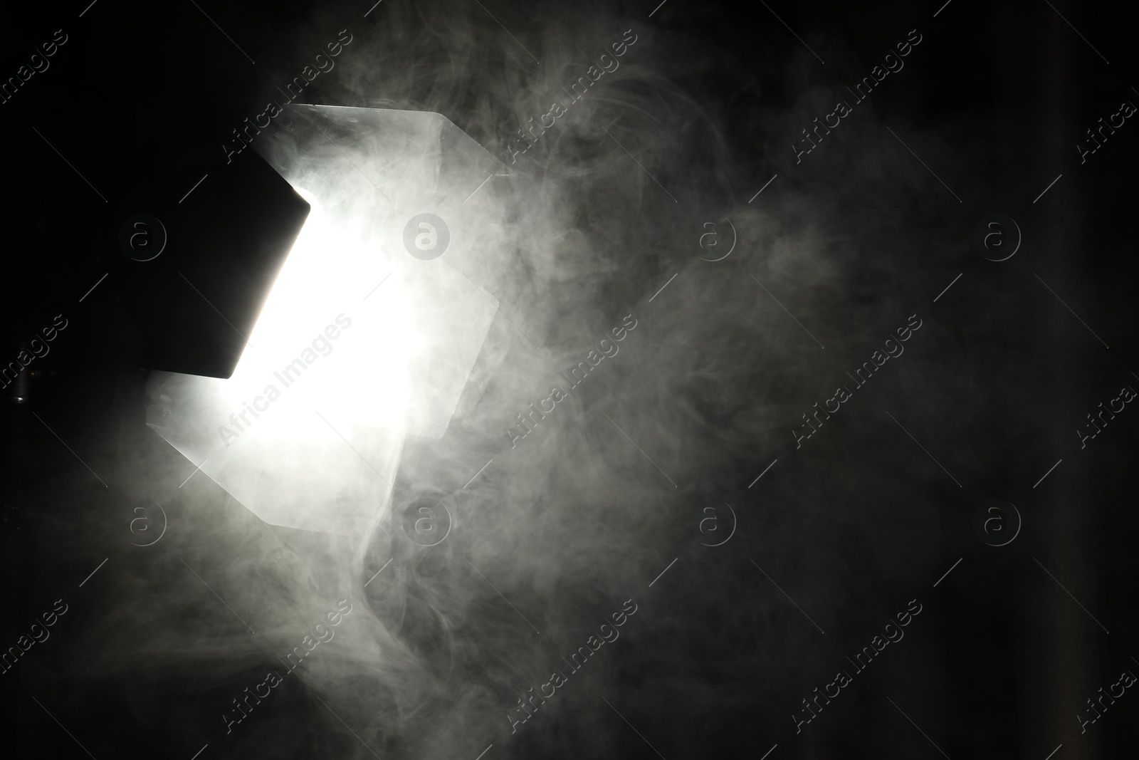 Photo of Professional spotlight and smoke against curtain in darkness. Space for text