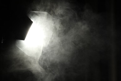 Photo of Professional spotlight and smoke against curtain in darkness. Space for text