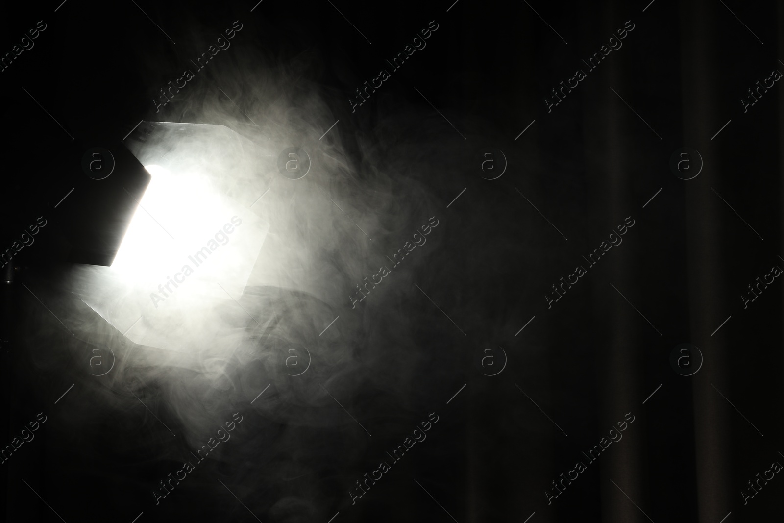 Photo of Professional spotlight and smoke against curtain in darkness. Space for text