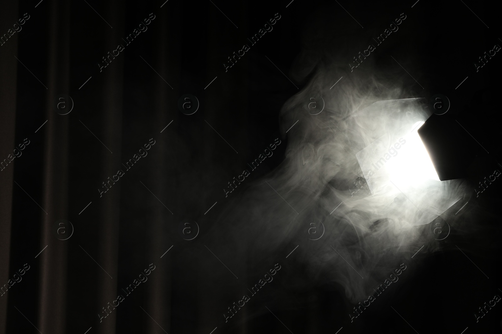 Photo of Professional spotlight and smoke against curtain in darkness. Space for text