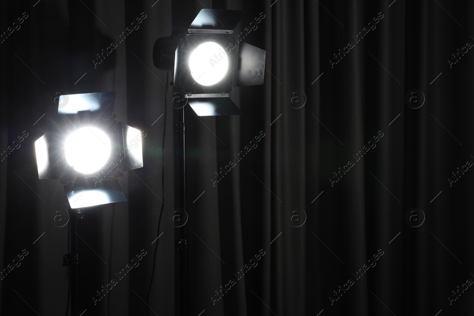 Photo of Professional spotlights against dark curtain. Space for text