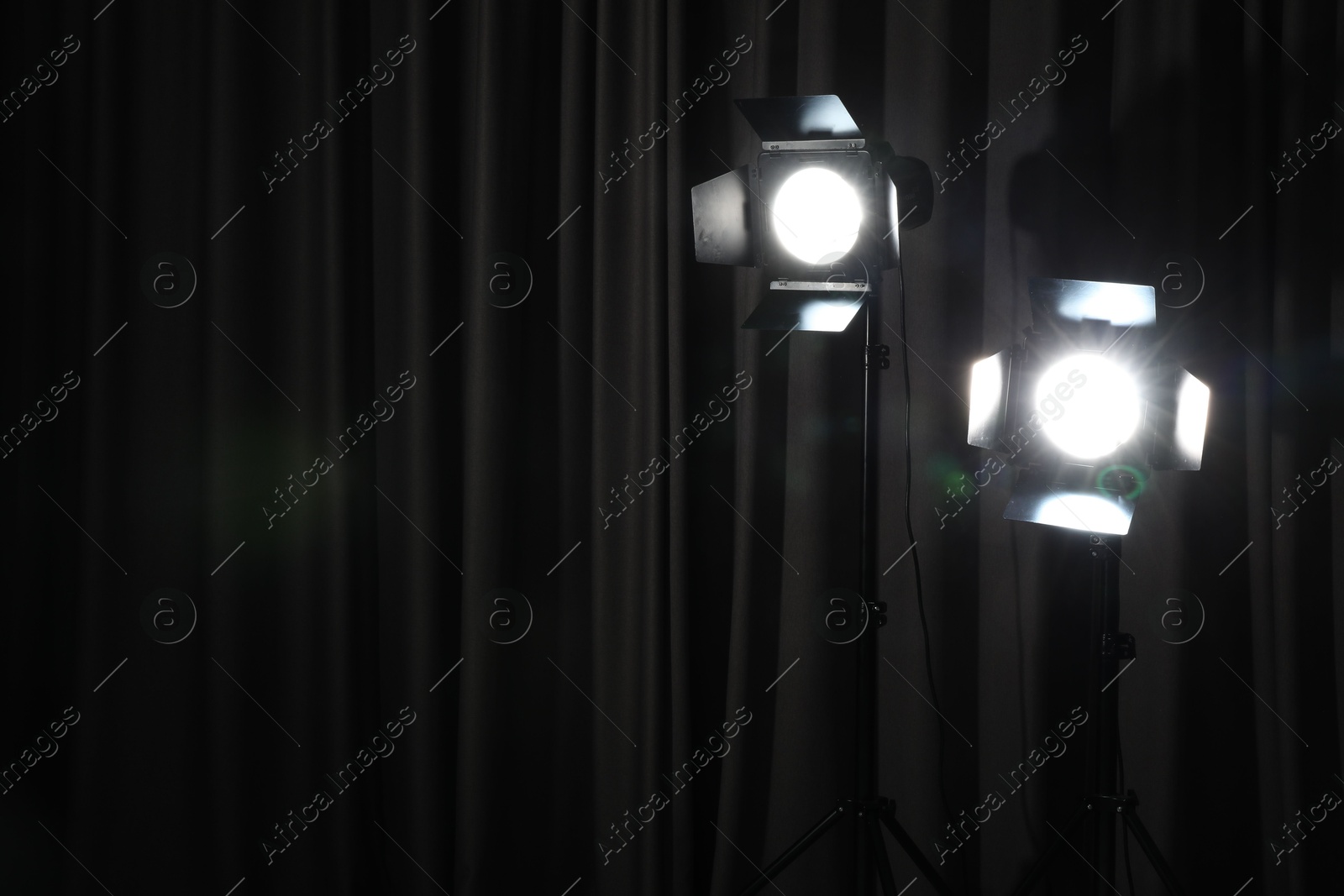 Photo of Professional spotlights against dark curtain. Space for text