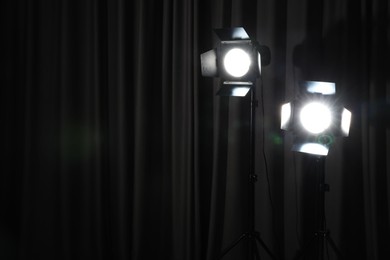 Photo of Professional spotlights against dark curtain. Space for text