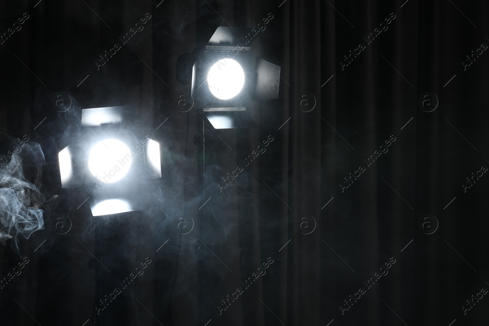 Photo of Professional spotlights and smoke against dark curtain. Space for text