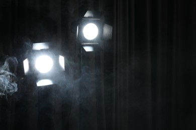 Photo of Professional spotlights and smoke against dark curtain. Space for text