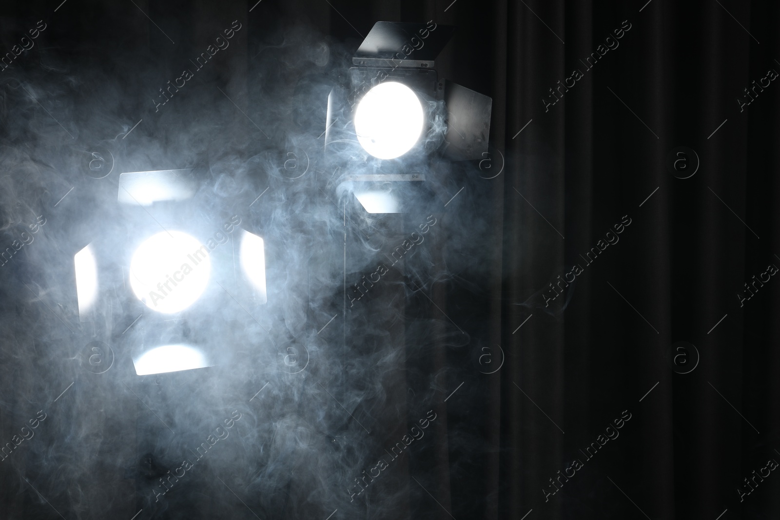 Photo of Professional spotlights and smoke against dark curtain. Space for text