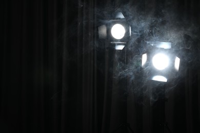 Photo of Professional spotlights and smoke against dark curtain. Space for text