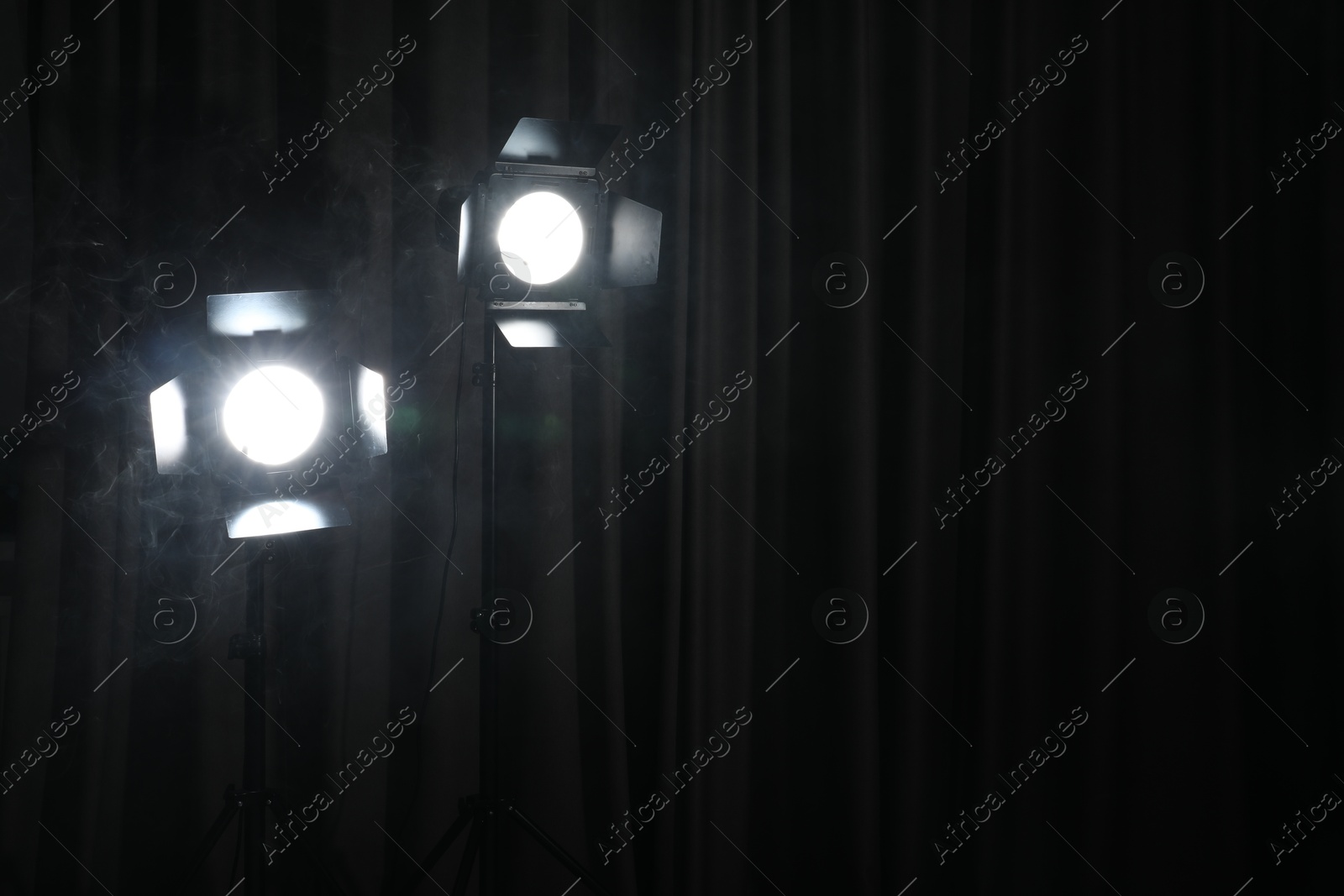 Photo of Professional spotlights and smoke against curtain in darkness. Space for text