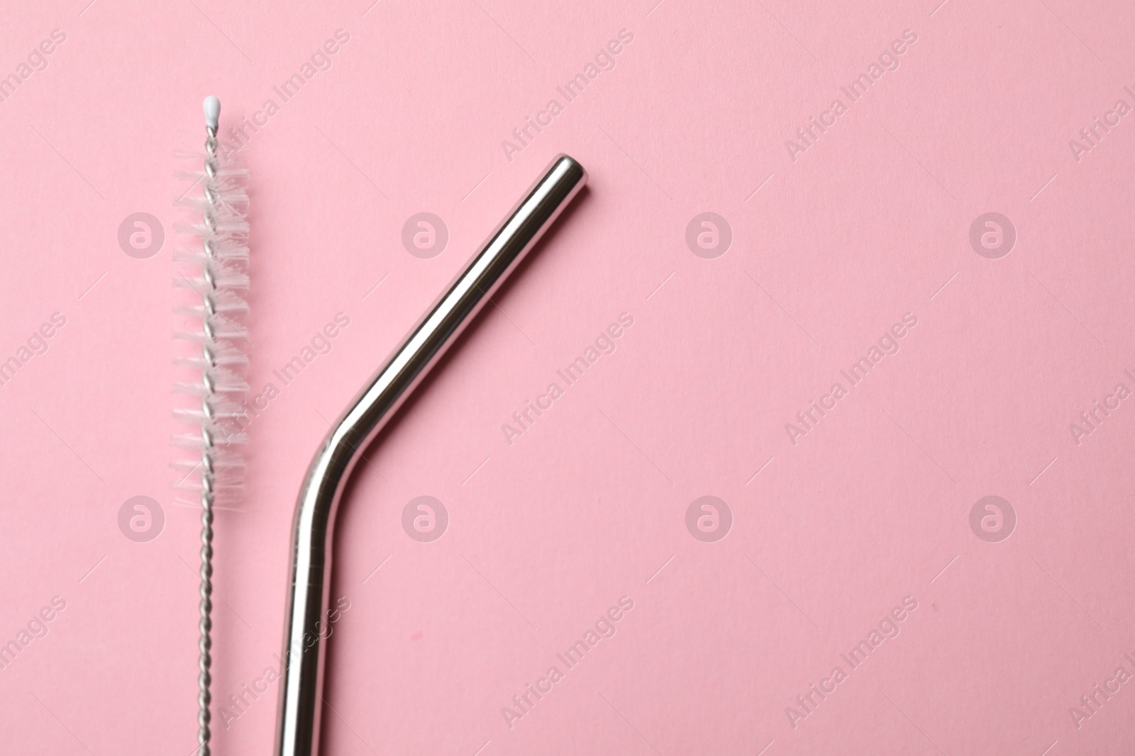 Photo of Metal drinking straw and cleaning brush on pink background, top view. Space for text