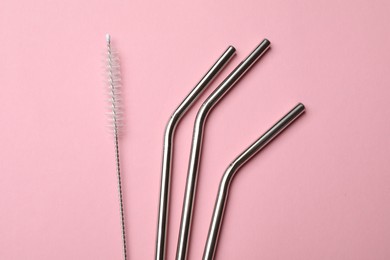 Photo of Metal drinking straws and cleaning brush on pink background, top view