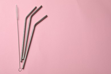 Photo of Metal drinking straws and cleaning brush on pink background, top view. Space for text