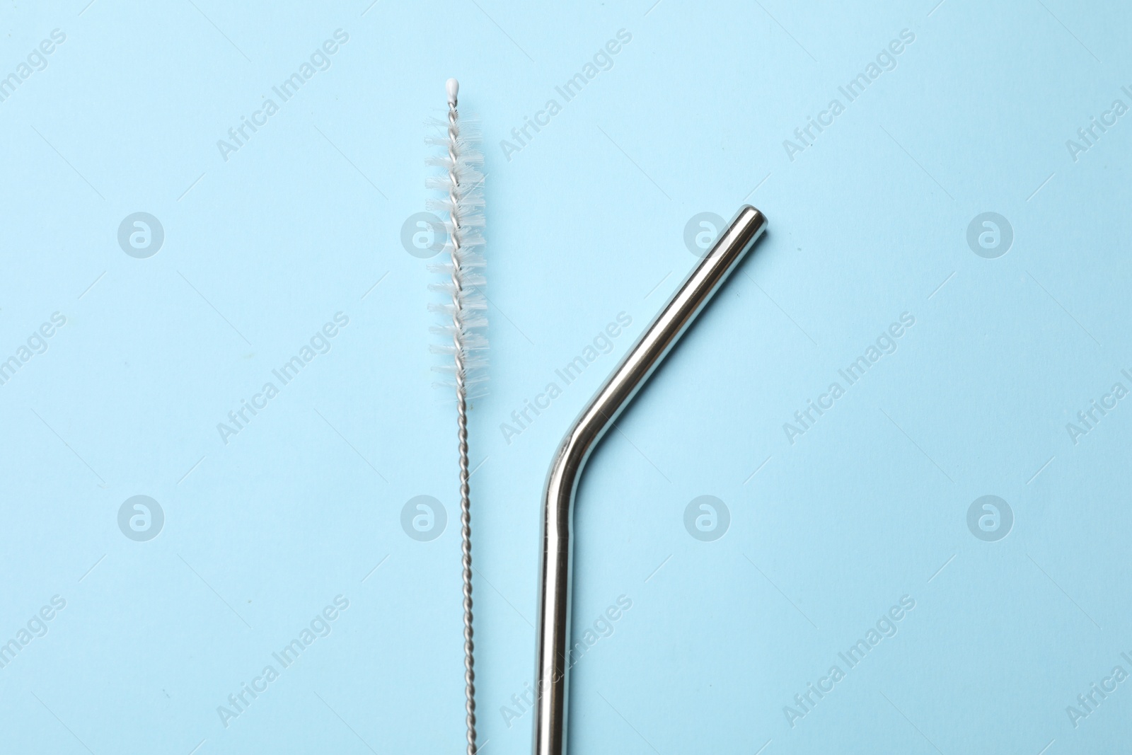 Photo of Metal drinking straw and cleaning brush on light blue background, top view