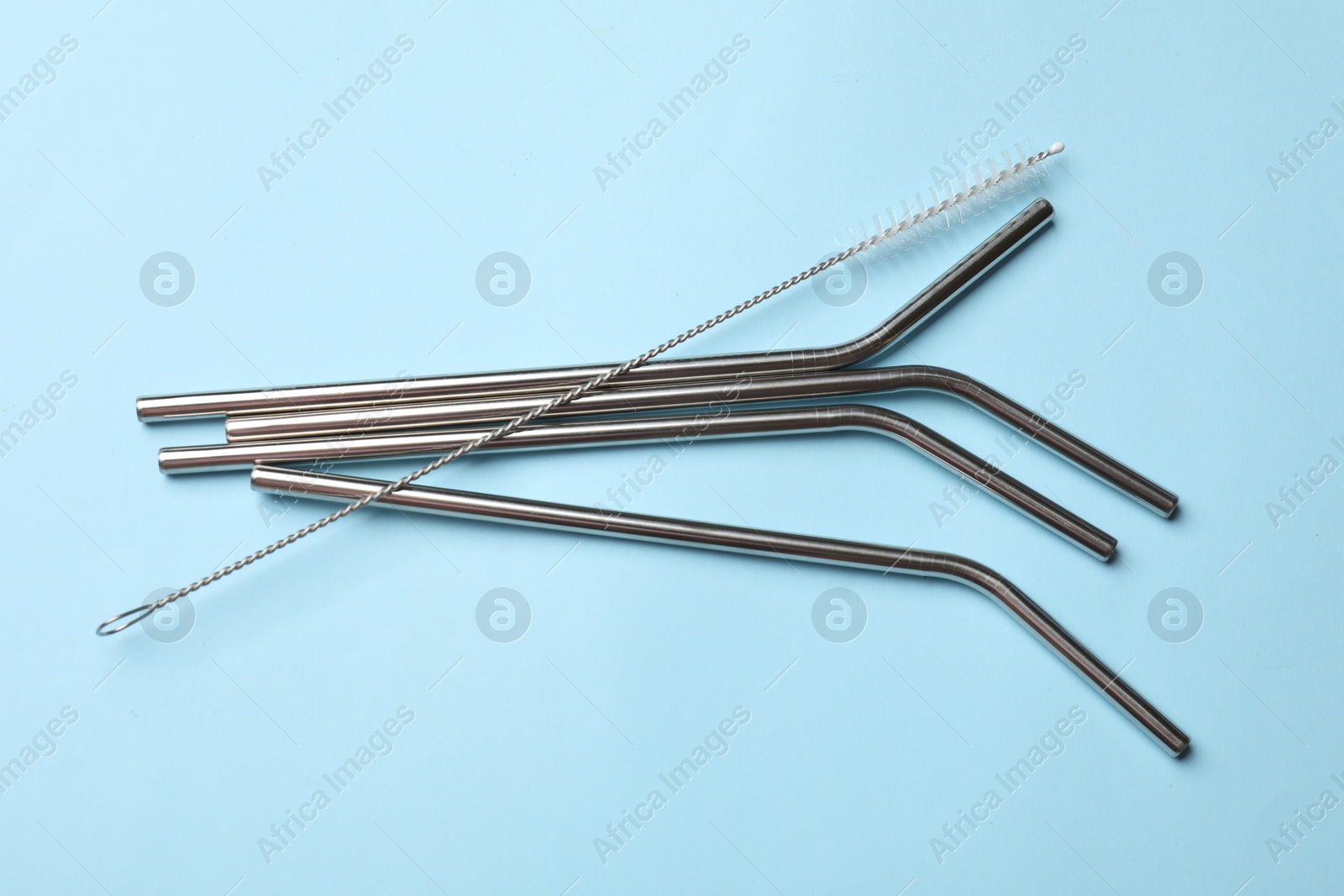 Photo of Metal drinking straws and cleaning brush on light blue background, top view