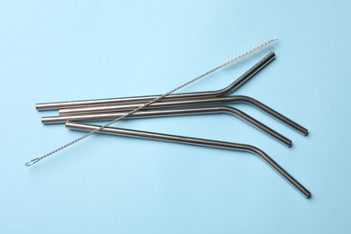 Photo of Metal drinking straws and cleaning brush on light blue background, top view