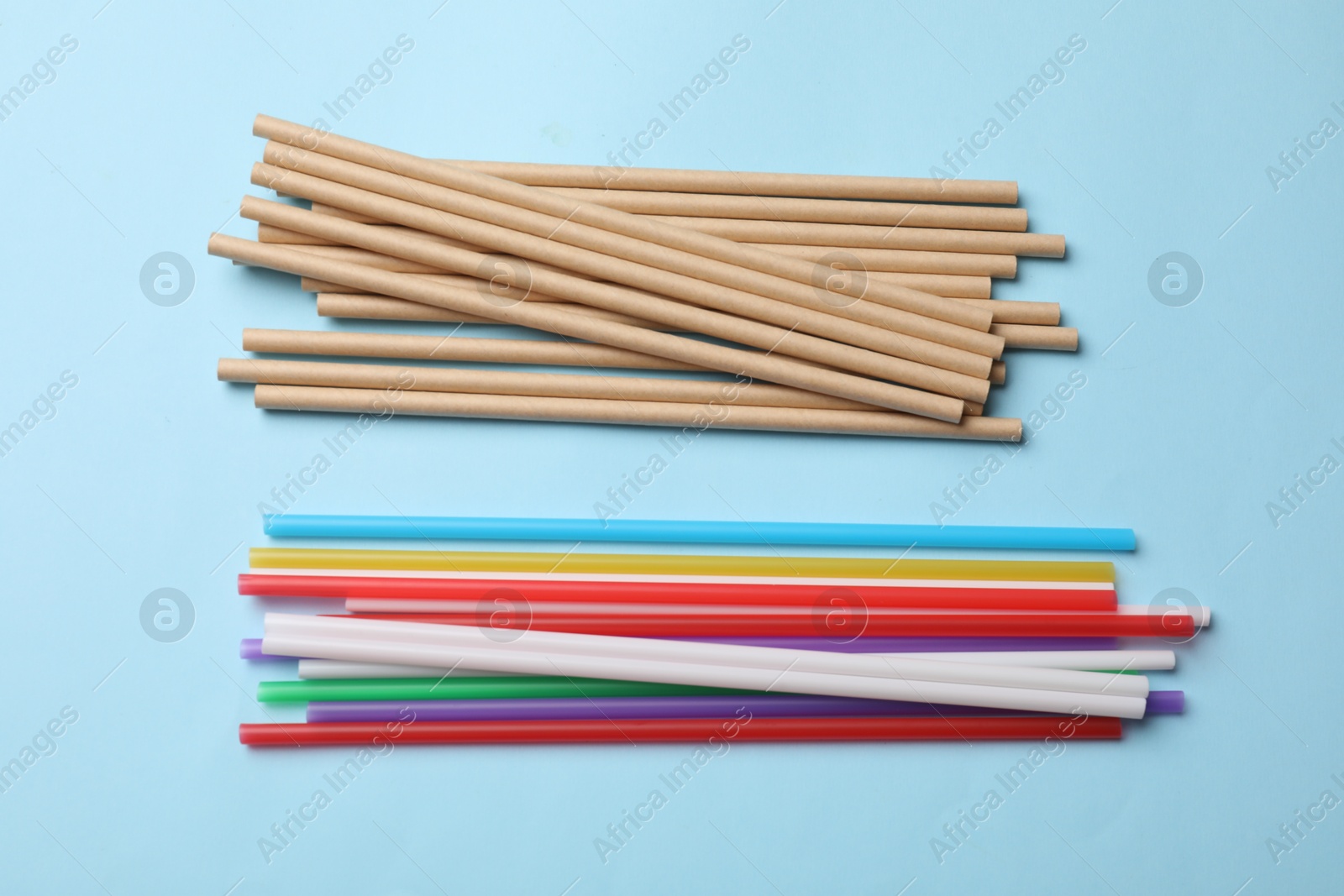 Photo of Plastic and bamboo drinking straws on light blue background, flat lay