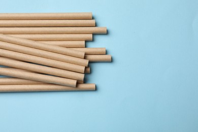 Photo of Bamboo drinking straws on light blue background, top view. Space for text