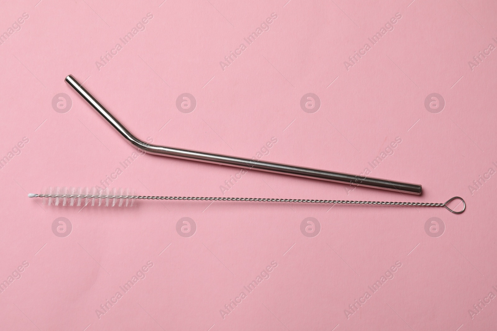 Photo of Metal drinking straw and cleaning brush on pink background, top view