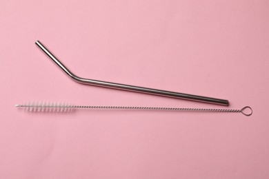 Photo of Metal drinking straw and cleaning brush on pink background, top view