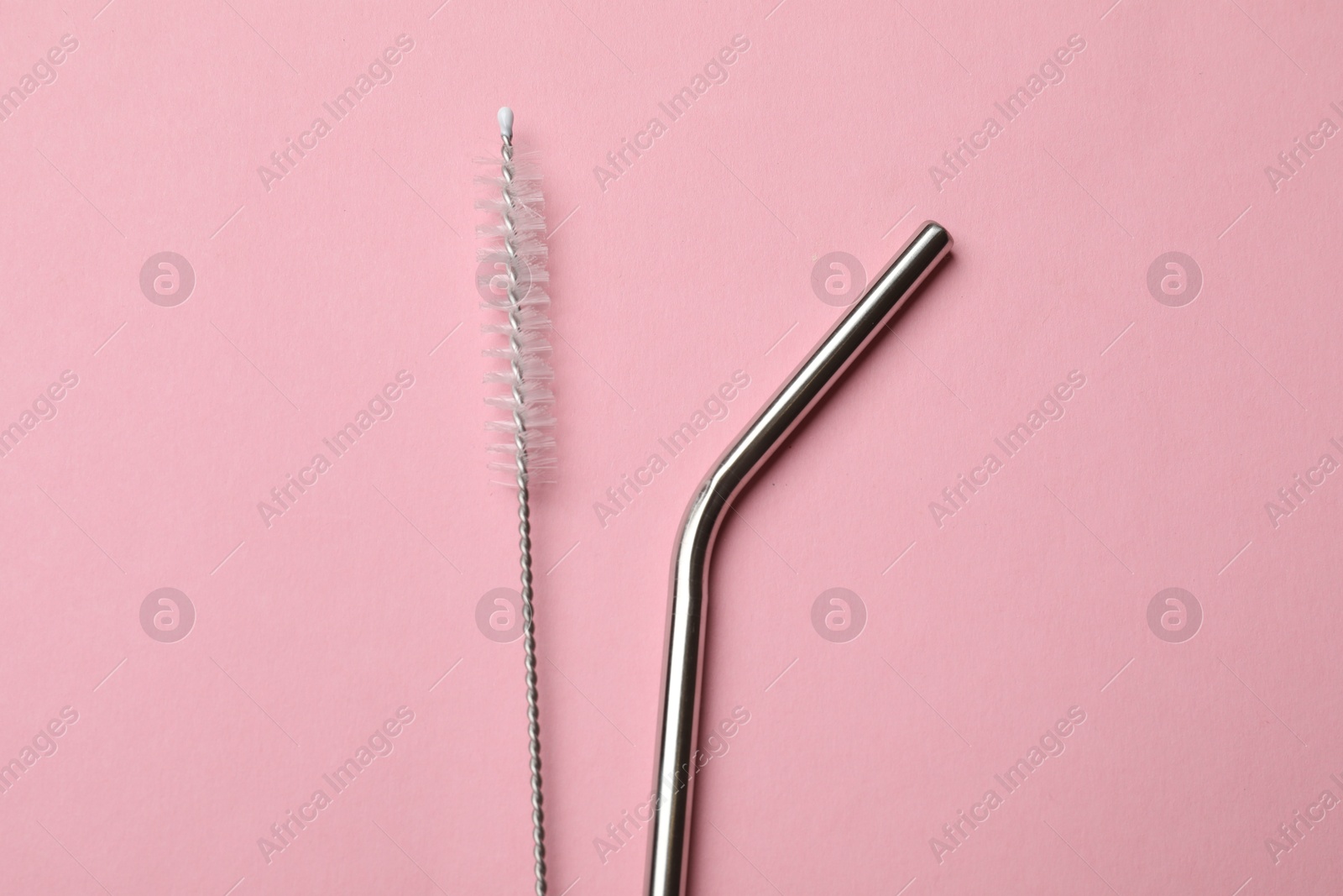 Photo of Metal drinking straw and cleaning brush on pink background, top view