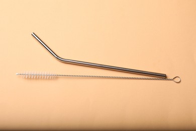 Photo of Metal drinking straw and cleaning brush on beige background, top view