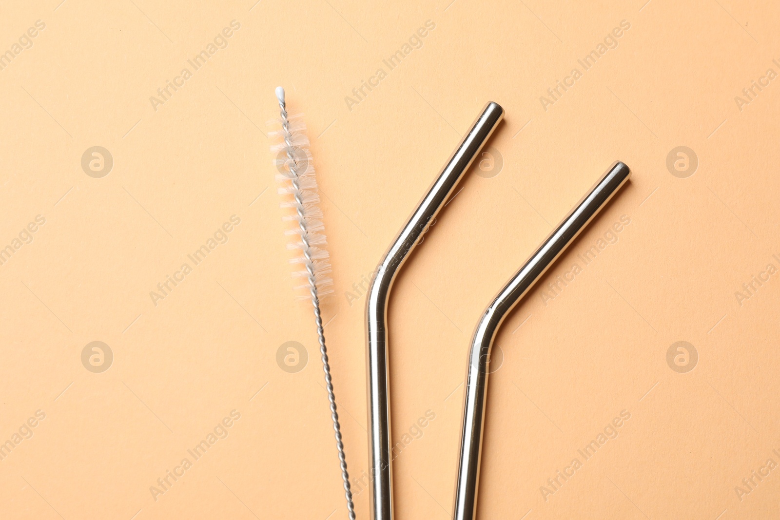 Photo of Metal drinking straws and cleaning brush on beige background, top view