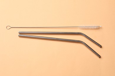 Photo of Metal drinking straws and cleaning brush on beige background, top view