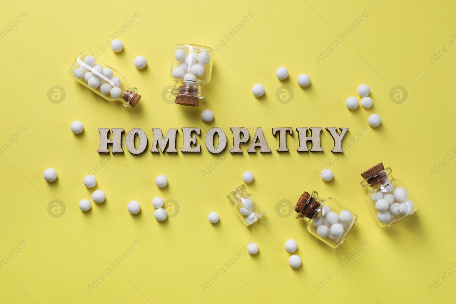 Photo of Word Homeopathy and pills on pale yellow background, flat lay