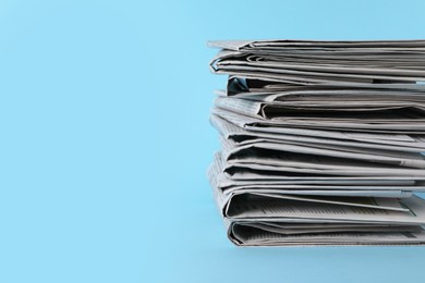 Photo of Stack of newspapers in different languages on light blue background. Space for text