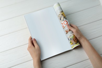 Woman reading magazine at white wooden table, top view. Mockup for design