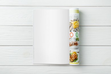 Open magazine with blank page on white wooden table, top view. Mockup for design