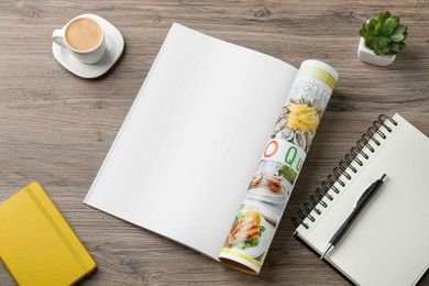 Photo of Open magazine with blank page, coffee, plant and stationery on wooden table, flat lay. Mockup for design