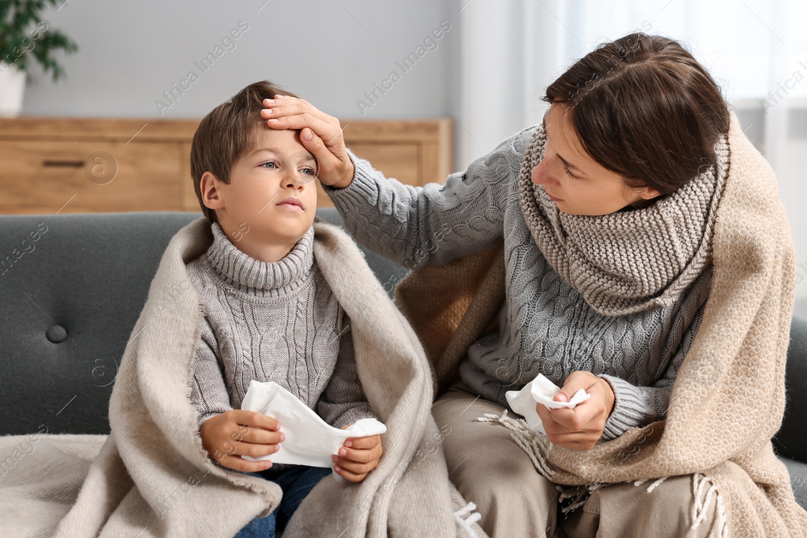 Photo of Cold symptom. Woman with her son suffering from fever on sofa at home