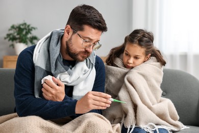 Cold symptom. Father with his daughter suffering from fever on sofa at home