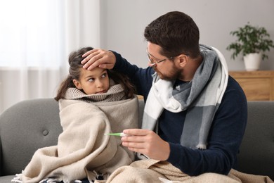 Cold symptom. Father with his daughter suffering from fever on sofa at home