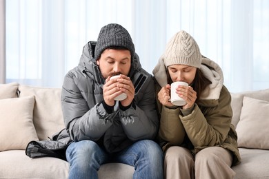 Photo of Cold symptom. Couple with cups of drink suffering from fever on sofa at home