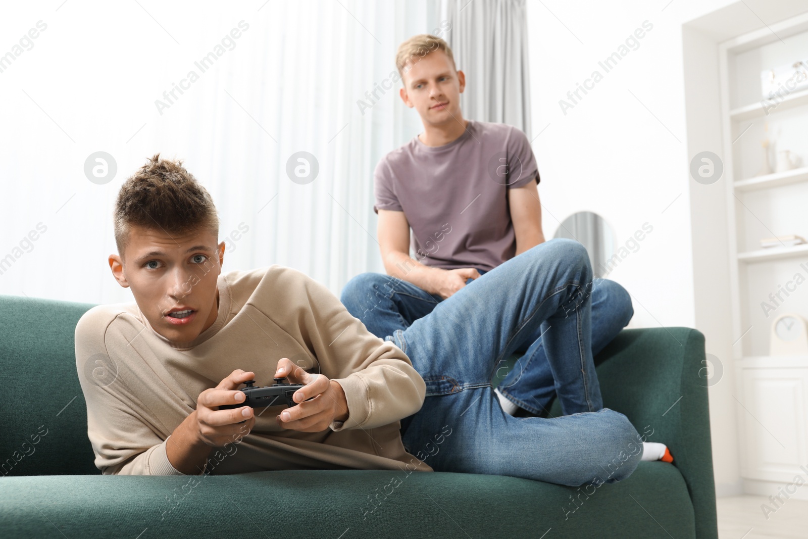 Photo of Young brothers playing video game on sofa at home, low angle view