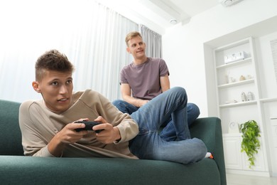 Photo of Young brothers playing video game on sofa at home, low angle view